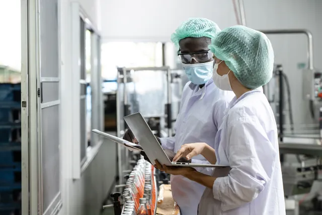 Two inspectors in PPE holding laptops while standing