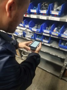 A logistics clerk uses a handheld device to issue parts management inventory in a maintenance storeroom.