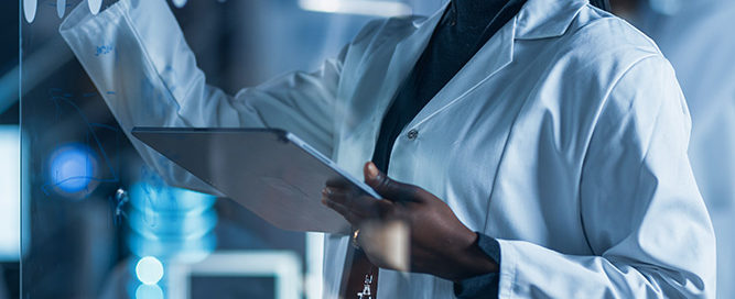 Woman wearing a white lab coat and looking at data using eMaint's computer systems validation software