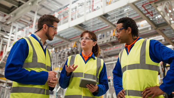 Arbeiter in einer Fabrik mit Schutzhelmen und Schutzwesten im Gespräch