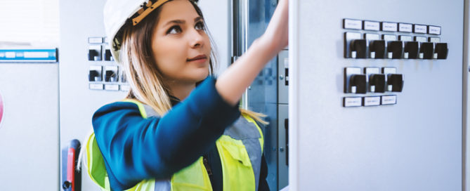 A facility maintenance engineer holding a tablet checks a control panel