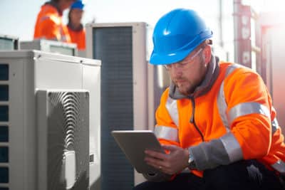 Technician uses facility management software on tablet while fixing AC units