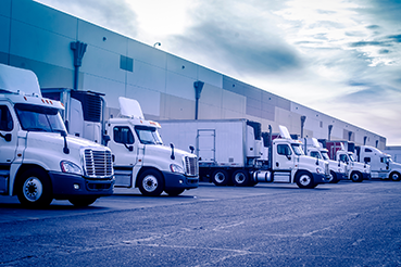 Uma frota de camiões estacionados numa instalação de distribuição. As empresas podem utilizar a gestão de património empresarial (EAM) para a manutenção da frota.
