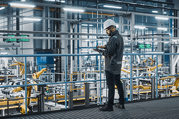 A man working in an automotive manufacturing facility where an enterprise asset management system (EAM) is being utilized.