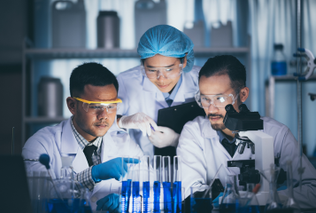 Três trabalhadores de laboratório a inspecionar o mesmo tubo de ensaio
