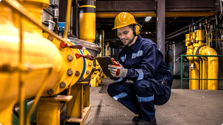 Trabajador de mantenimiento con casco amarillo consultando una tableta mientras se arrodilla