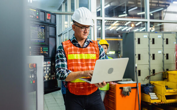 Trabalhador da manutenção com um capacete branco a utilizar um software de gestão de instalações num computador.